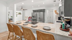 A modern kitchen with a central island, stainless steel appliances, and a dining area with wicker chairs. - Fresno House - Pool + Arcade Games , Family Friendly! (Fresno)