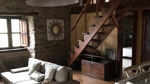 A rustic interior with a wicker sofa, a wooden staircase, and a stone wall. - Rural House 'O Paxar' with Mountain Views, Private Terrace and Wi-Fi (SAMOS)