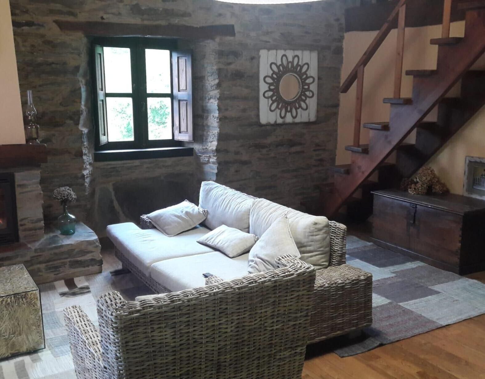 Un salon chaleureux avec une cheminée en pierre, un canapé en osier, un escalier en bois et un élément décoratif mural.