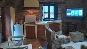 A rustic kitchen with stone walls, a wooden cabinet, a white refrigerator, a sink, and a television mounted on the wall. - Rural House 'O Paxar' with Mountain Views, Private Terrace and Wi-Fi (SAMOS)
