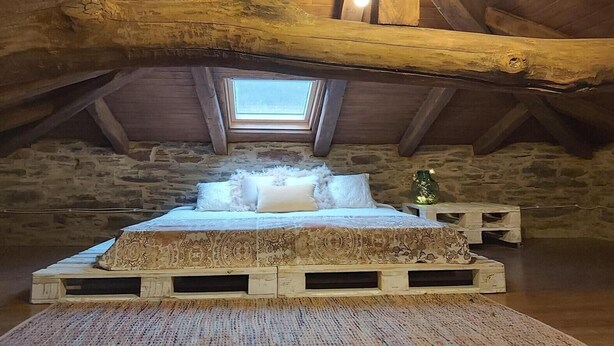 A rustic attic bedroom with a sloped ceiling, a skylight, a wooden bed with patterned bedding, and a stone wall. - Rural House 'O Paxar' with Mountain Views, Private Terrace and Wi-Fi (SAMOS)