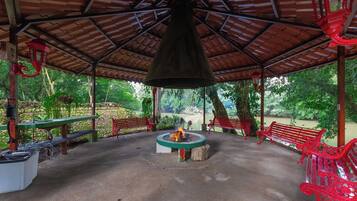 A covered outdoor area with a fire pit, benches, and a view of a river.