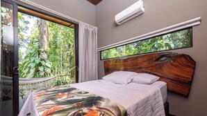 Un dormitorio con una cama grande, vista a espacios verdes a través de una ventana y un equipo de aire acondicionado en la pared.