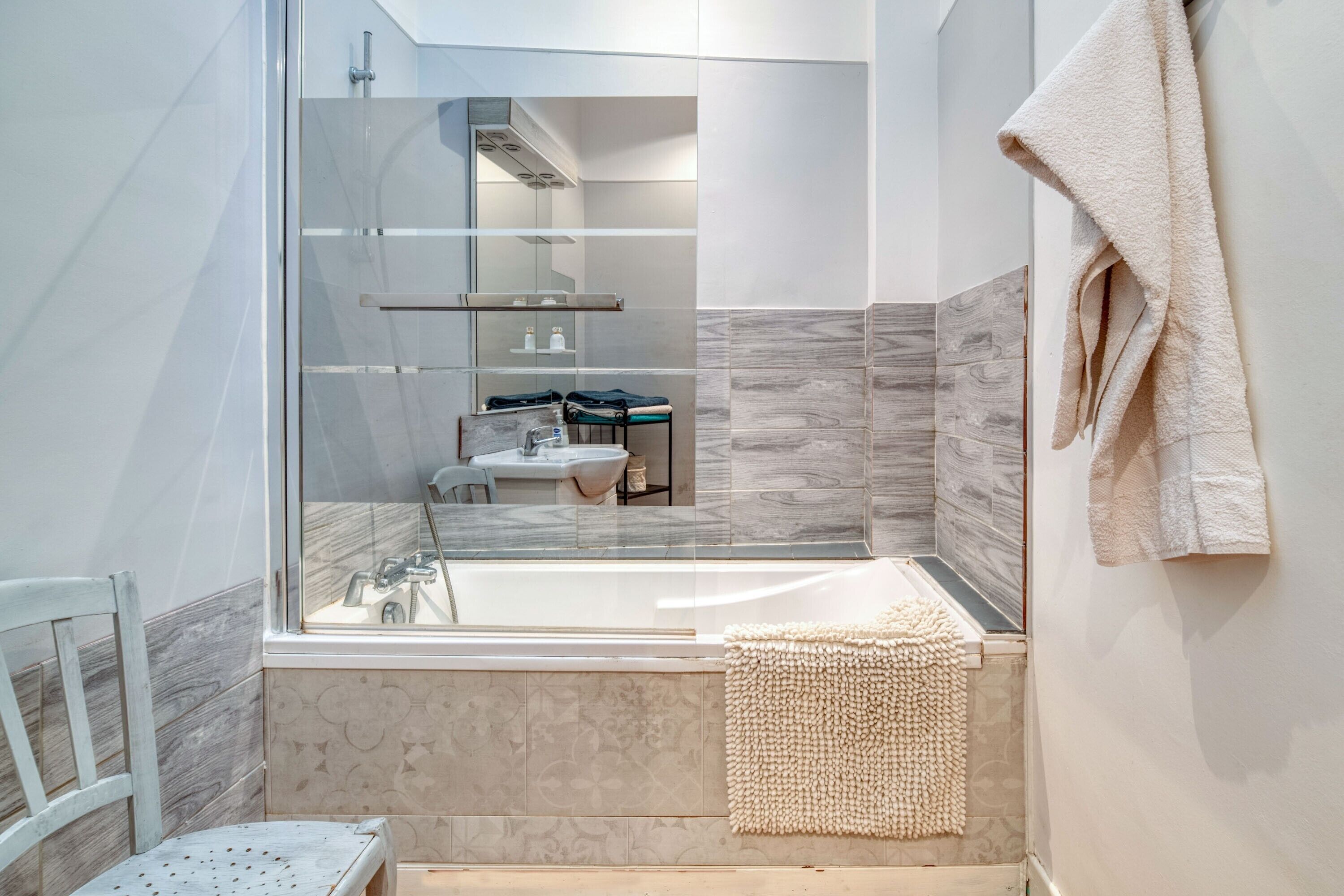 Une salle de bain moderne dotée d’une douche à parois de verre, d’une baignoire et d’un espace cuisine visible à travers le verre.