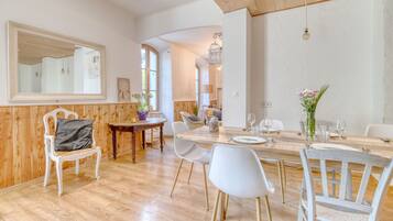 Un coin repas avec une table en bois, des chaises blanches et un grand miroir au mur.