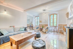 Un grand espace de vie comprenant un canapé, une table basse et des fauteuils, une table à manger avec des chaises, ainsi qu’un coin cuisine équipé d’un réfrigérateur.
