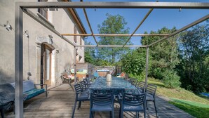 An outdoor patio with a wooden deck, a covered table with chairs, and a stone wall. - Holiday Home 'Maison Avec Piscine Et Remous' with Private Pool, Terrace and Wi-Fi (Revel)
