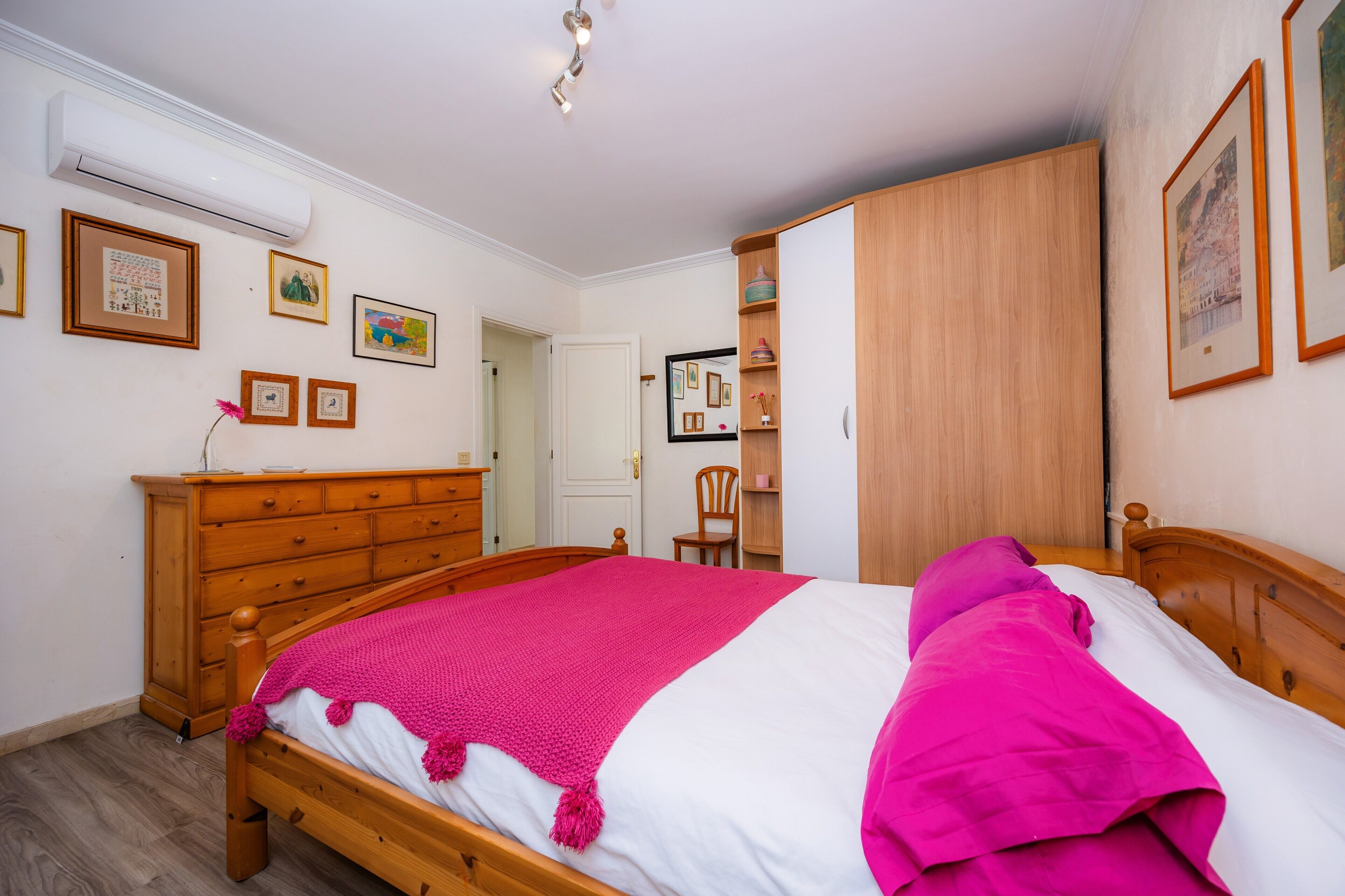 Une chambre à coucher avec un lit en bois, une commode, une armoire et des tableaux encadrés accrochés au mur.