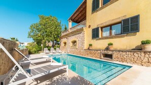 Ein Schwimmbecken mit Liegestühlen, einer Steinmauer und einem Gebäude mit Fensterläden.