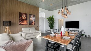 A modern dining area with a wooden table, black chairs, a white sofa, and a large TV on the wall. - Brand-New Villa 'Carlota' with Sea Views, Private Pool & Wi-Fi (garachico)