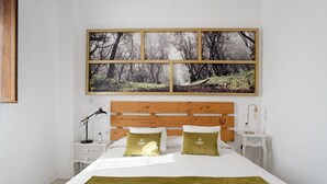Een slaapkamer met een houten hoofdbord, een groot kunstwerk met bosmotieven, twee kussens, een nachtkastje met een lamp en een lade.