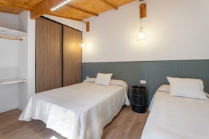 Ein Zimmer mit zwei Betten, Holzboden, einem Kleiderschrank und Pendelleuchten.