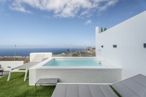 Un área de piscina moderna al aire libre con vista al océano, paredes blancas y cielo despejado.