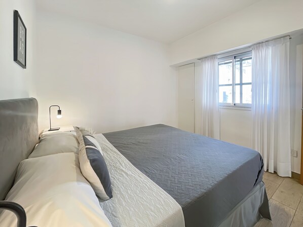 A bedroom with a bed, bedside table, lamp, and a window with curtains.
