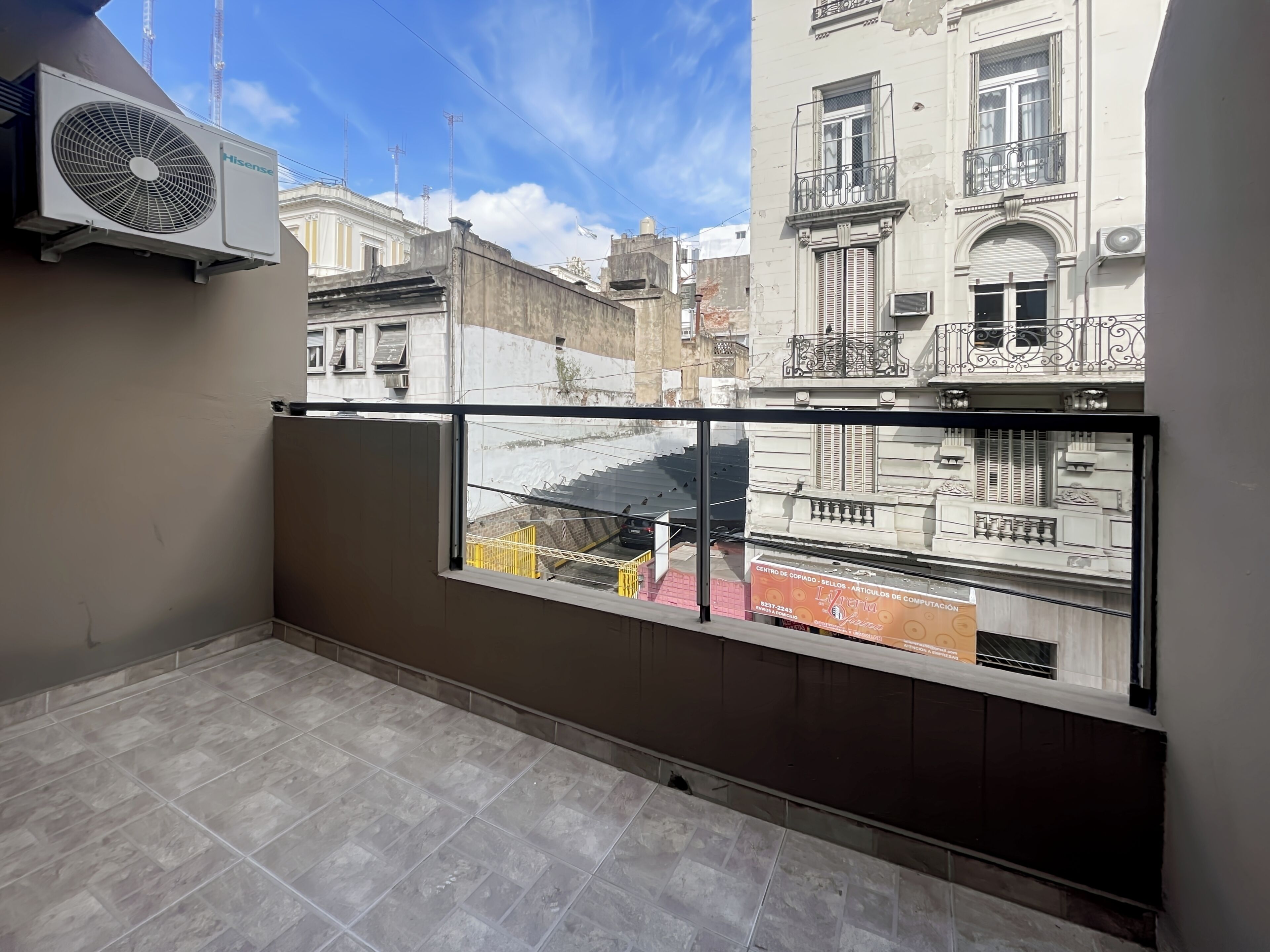 Balkon med udsigt til ældre bygninger, en Hisense aircondition og et flisegulv.