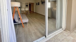 Un apartamento moderno con un ventanal corredero que da a un balcón, un sofá, un comedor y una cocina.
