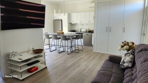 Ein modernes Wohnzimmer mit grauem Sofa, einem Flachbildfernseher und einem Essbereich, im Hintergrund befindet sich eine Küche.