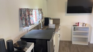 Uma cozinha compacta com bancada preta, pia e janela com cortinas florais.