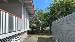 Um espaço ao ar livre cercado por uma mureta, com um caminho de cascalho, vegetação e um edifício com fachada branca e detalhes vermelhos.