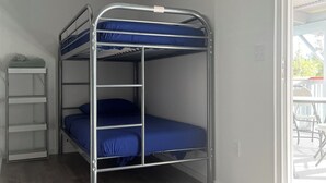 Uma cama beliche com estrutura metálica e roupa de cama azul em quarto com piso de madeira e parede branca.