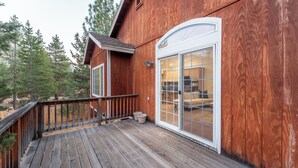 A wooden deck with a railing, a large sliding glass door leading to a living area, and a view of the surrounding forest. - Blitzen by Avantstay Pet-friendly Tahoe Retreat, Near Heavenly Ski Resort (South Lake Tahoe)