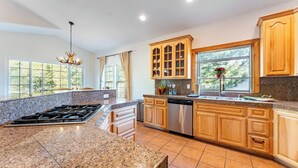 A kitchen with granite countertops, wooden cabinets, a stainless steel dishwasher, and a window with a view of trees. - Blitzen by Avantstay Pet-friendly Tahoe Retreat, Near Heavenly Ski Resort (South Lake Tahoe)