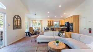 A modern living room with a large sectional sofa, a dining area with chairs, and a kitchen with wooden cabinets and appliances. - Blitzen by Avantstay Pet-friendly Tahoe Retreat, Near Heavenly Ski Resort (South Lake Tahoe)