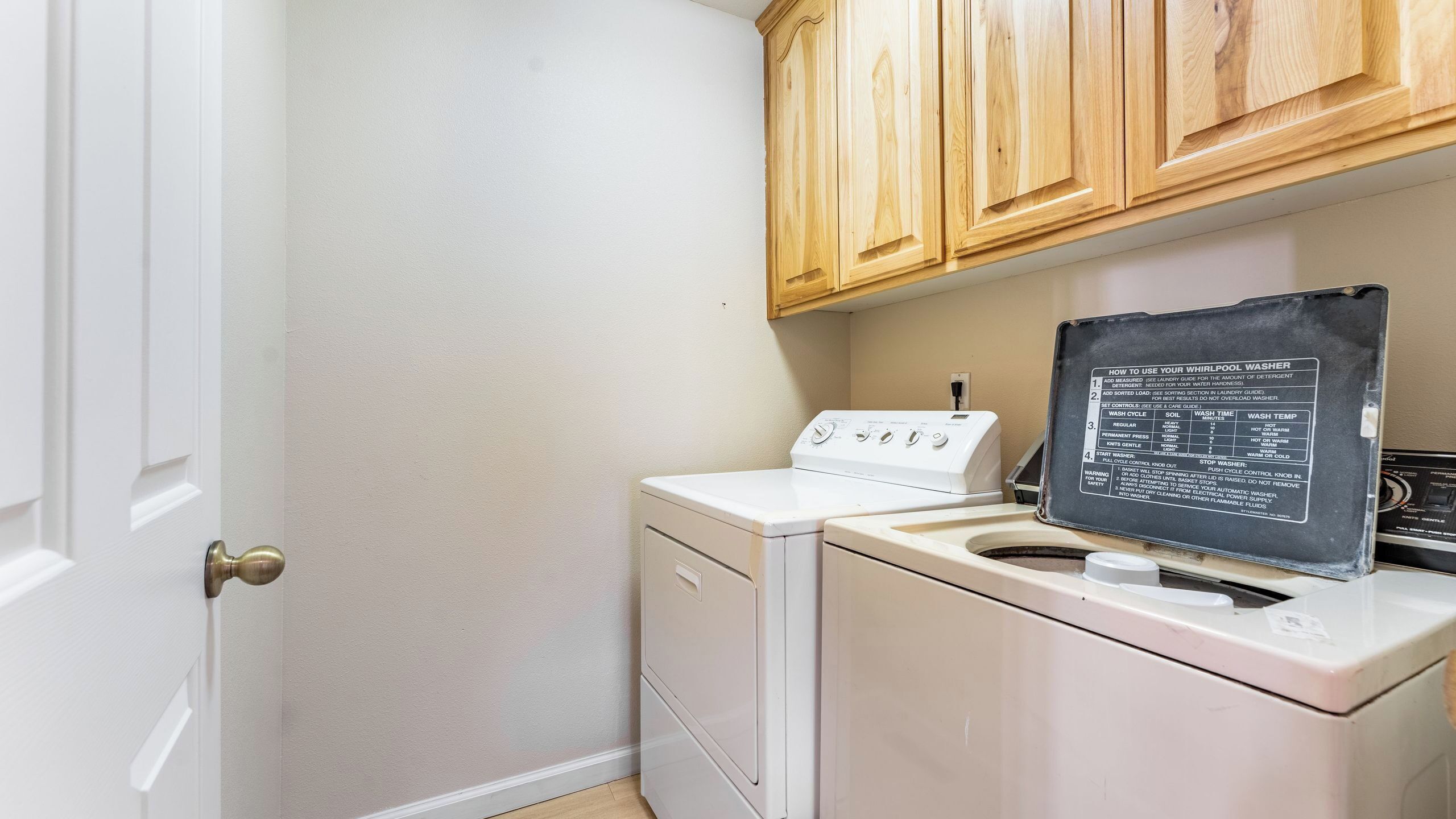 A laundry room with a washing machine, dryer, and wooden cabinets.