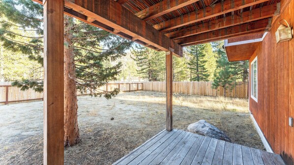 Una terraza de madera con una pérgola, un patio cercado y un árbol grande.