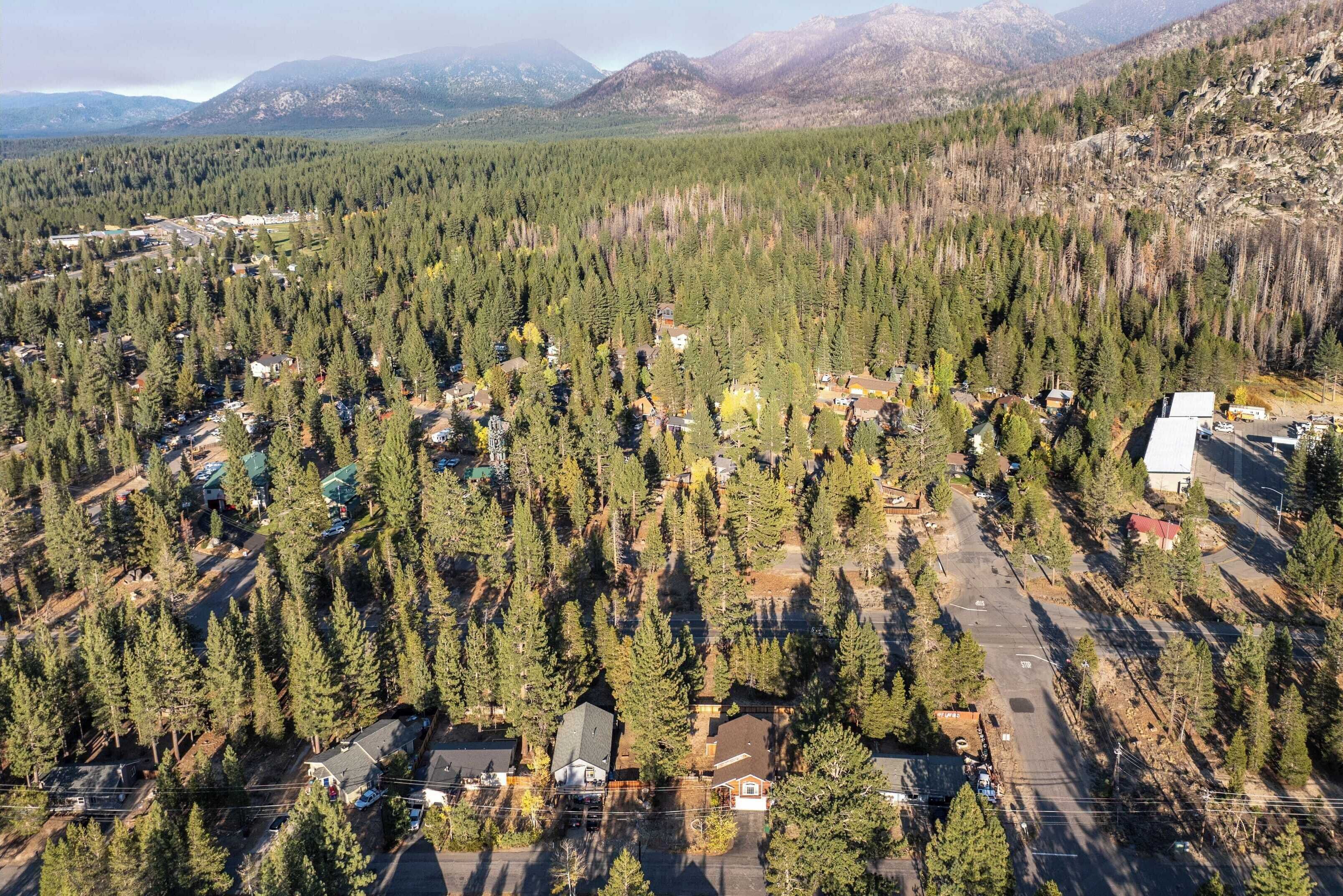 An aerial view of a residential area with houses surrounded by dense forests and mountains in the background.