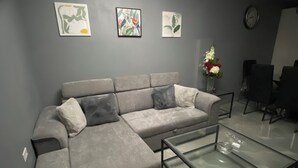 En moderne stue med en grå hjørnesofa, et glas sofabord og billedkunst på væggen.
