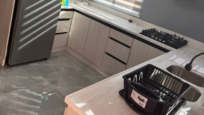 Et moderne køkken med et rustfrit stål køleskab, en gasblus og en sort opvaskestativ på bordet.