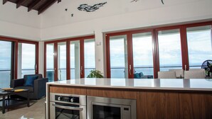 Eine geräumige Küche mit einer großen Kochinsel, Holdschränken und Edelstahlgeräten. Große Fenster bieten Blick auf das Meer.