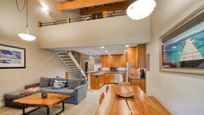A spacious living area with a wooden dining table, grey sofa, and a staircase leading to an upper level.