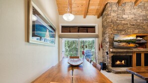 A dining area with a wooden table, chairs, a stone fireplace, and a view through the glass doors.