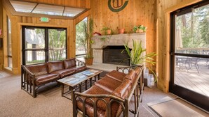 A wooden interior with a fireplace, leather sofas, and a large window overlooking a deck.