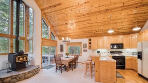 A spacious kitchen with wooden cabinets, a stone fireplace, and large windows.