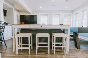 A modern kitchen with a central island, bar stools, and a large flat-screen TV. - Coastal Distancing: Oceanside, Private Pool, Hot Tub, Close to Beach (Nags Head)