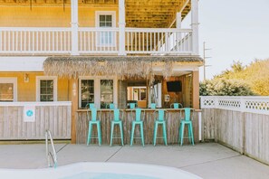 A two-story building with a wooden balcony and a thatched roof over a bar area with turquoise chairs. - Coastal Distancing: Oceanside, Private Pool, Hot Tub, Close to Beach (Nags Head)