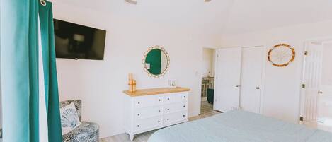 A bedroom with a bed, a dresser, a mirror, a ceiling fan, and a TV on the wall.