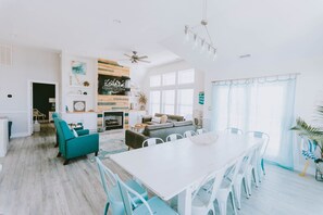 A spacious living area with a dining table, teal chairs, and a sofa. - Coastal Distancing: Oceanside, Private Pool, Hot Tub, Close to Beach (Nags Head)