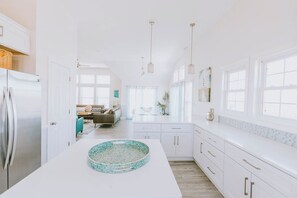 A modern kitchen with white cabinetry, a central island with a decorative bowl, and pendant lighting. - Coastal Distancing: Oceanside, Private Pool, Hot Tub, Close to Beach (Nags Head)