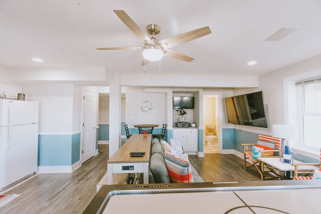 A modern kitchen with a dining area, a ceiling fan, and a TV mounted on the wall.
