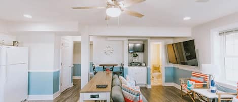 A modern kitchen with a dining area, a ceiling fan, and a TV mounted on the wall.