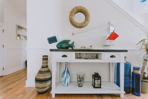 A white console table with drawers, a wicker wall hanging, a small desk lamp, and a red notebook. - Coastal Distancing: Oceanside, Private Pool, Hot Tub, Close to Beach (Nags Head)