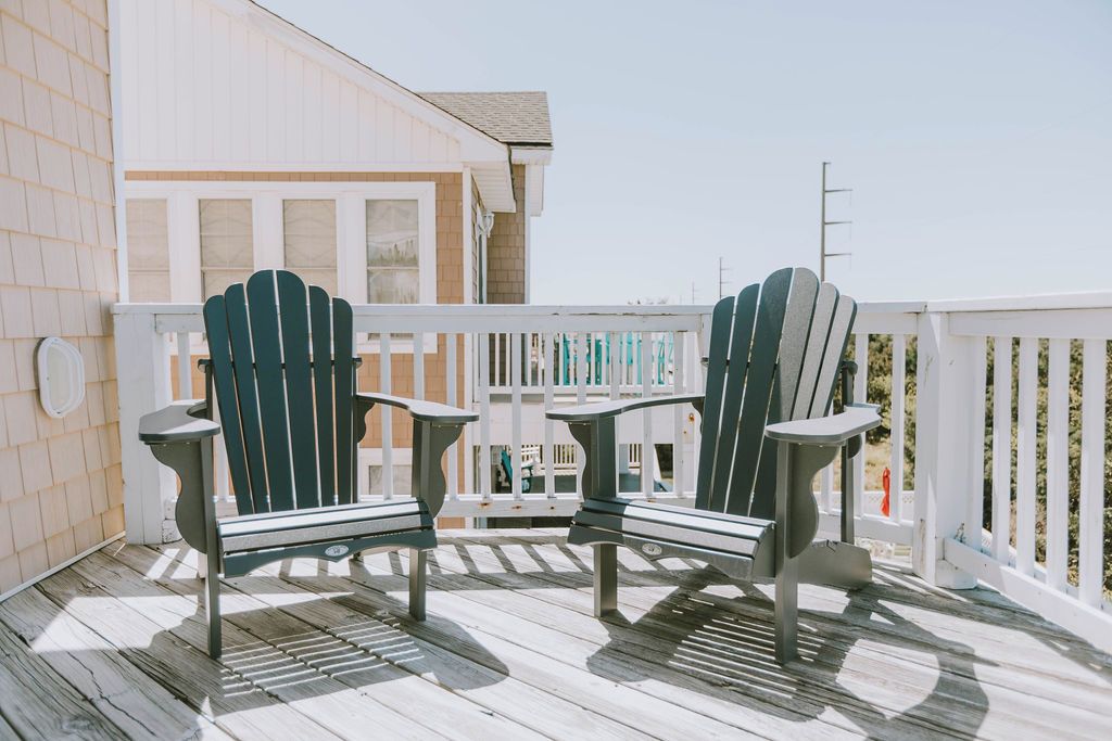 A wooden deck with two Adirondack chairs and a small table.