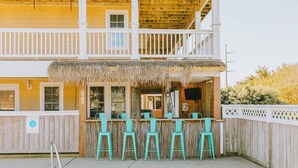A two-story building with a wooden balcony and a thatched roof over a bar area with turquoise chairs. - Coastal Distancing: Oceanside, Private Pool, Hot Tub, Close to Beach (Nags Head)