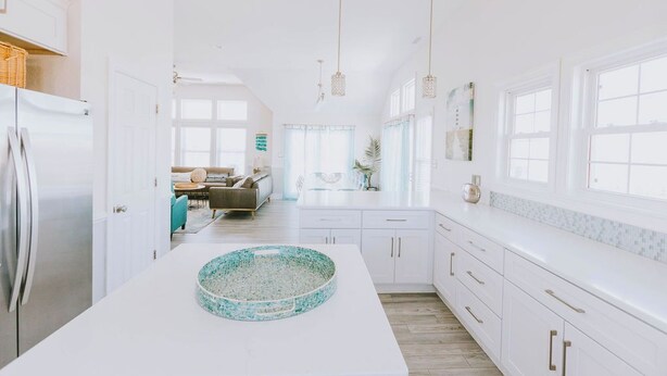 A modern kitchen with white cabinetry, a central island with a decorative bowl, and pendant lighting. - Coastal Distancing: Oceanside, Private Pool, Hot Tub, Close to Beach (Nags Head)