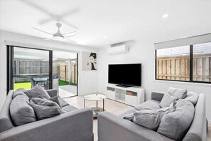 Relax in this stylish living room with a large flat-screen TV, comfortable sofas, and a sliding door to an outdoor area.