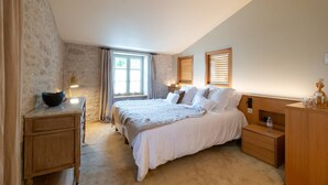 A bedroom with a large bed, wooden nightstands, a bedside table with a lamp, and a window with curtains. - Grande Bellezza - Renovated village houses designed like a hotel (ARS EN RE)